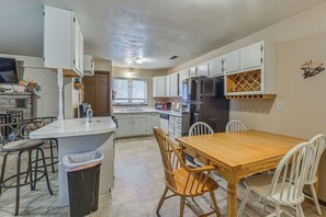 A kitchen with white cabinets, a central island with stools, a dining table with chairs, and a refrigerator. - Ruidoso Retreat w/ Grill ~ 3 Mi to Grindstone Lake (Ruidoso)