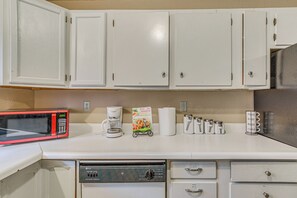 A kitchen with white cabinets, a red microwave, a coffee maker, and a paper towel holder.