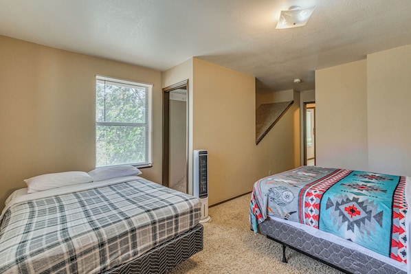 A bedroom with two beds, a window, a mirror, a heater, and a staircase.