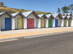 A row of beach huts with numbered doors, each with a different color, and a clear sky in the background.