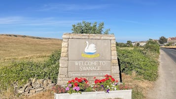 Placa de boas-vindas do Conselho da Cidade de Swanage, com um logotipo de cisne, acompanhada por um muro de pedra e canteiro de flores.