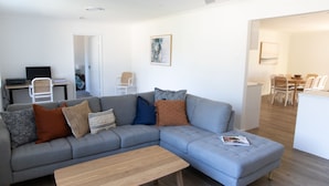 Ein modernes Wohnzimmer mit einem grauen Ecksofa, einem Holztisch und einem Essbereich mit weißem Tisch und Stühlen.