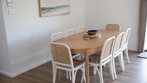 Ein Essbereich mit einem runden Holztisch, umgeben von weißen Stühlen mit gewebten Sitzflächen.