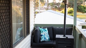 Ein Balkon mit einer schwarzen Couch, einem gemusterten Kissen und einem kleinen Tisch mit einem Mikrofon.