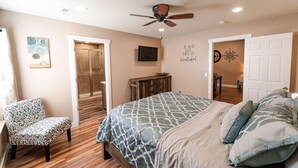 Une chambre à coucher comprenant un lit, une chaise, une armoire, un ventilateur de plafond et un mur orné d’une citation inspirante.