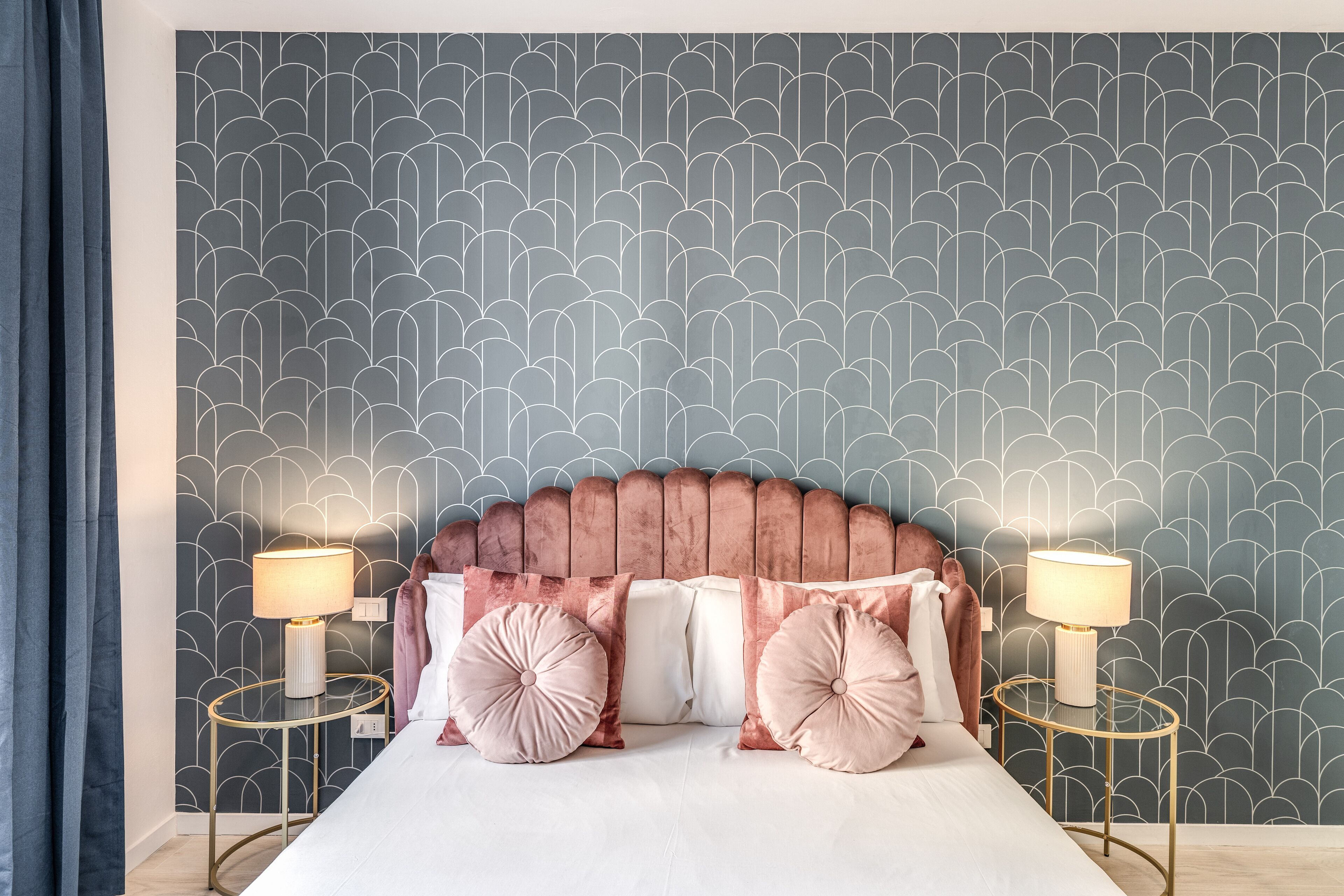 A bedroom with a patterned wallpaper, a large bed with multiple pillows, and two bedside lamps.