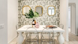 Un comedor con una mesa blanca, sillas transparentes y un papel tapiz con estampado geométrico.