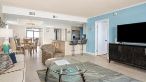 A spacious living area with a glass coffee table, a sofa, a dining area with chairs, and a kitchen in the background.