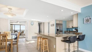 A modern kitchen with a central island, bar stools, and a dining area with wooden chairs.