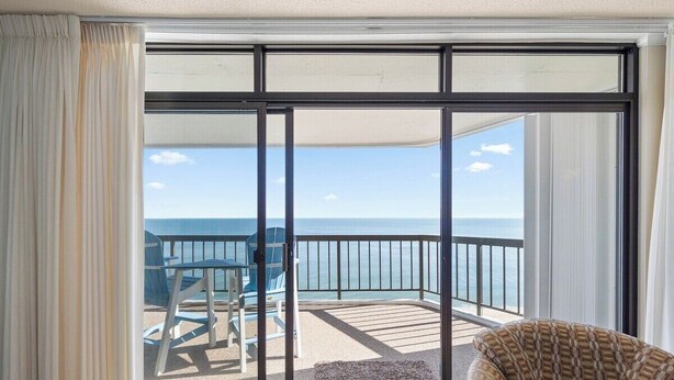 A balcony with a view of the sea, a chair, and a table.