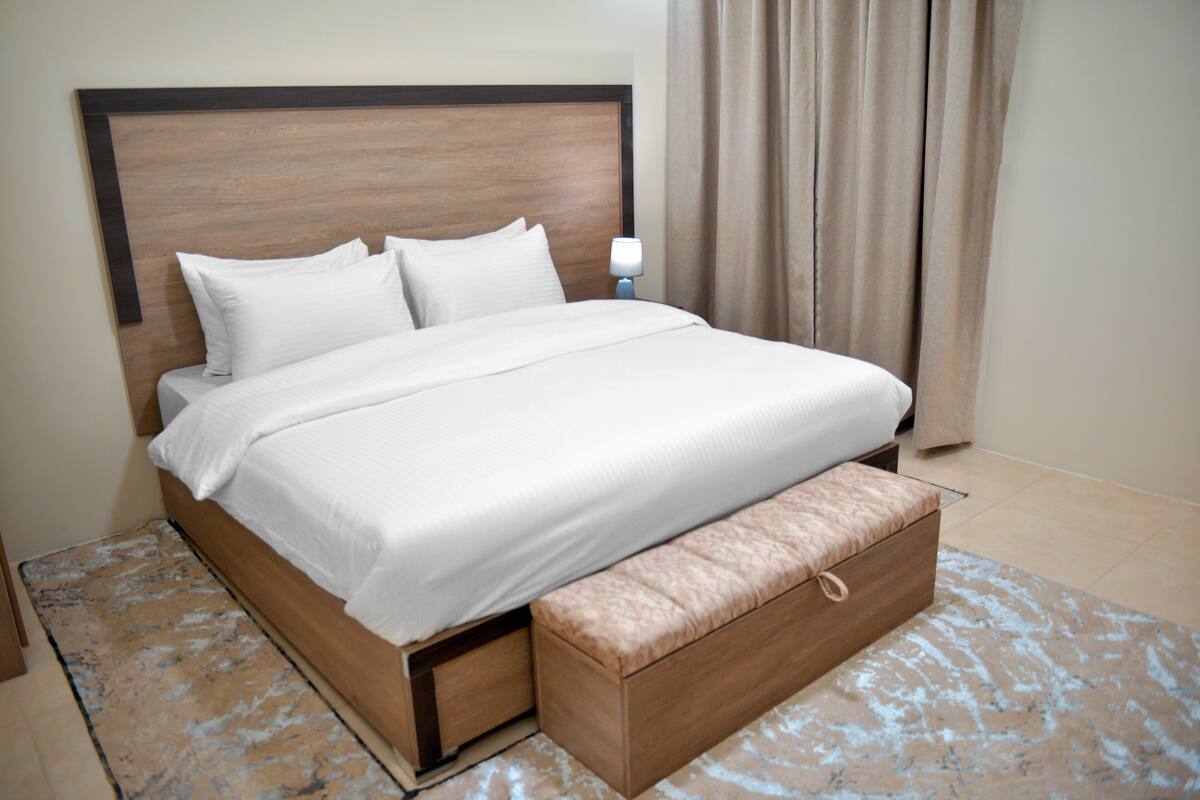 A neatly made bed with a wooden headboard, a bedside lamp, and a bench at the foot of the bed.