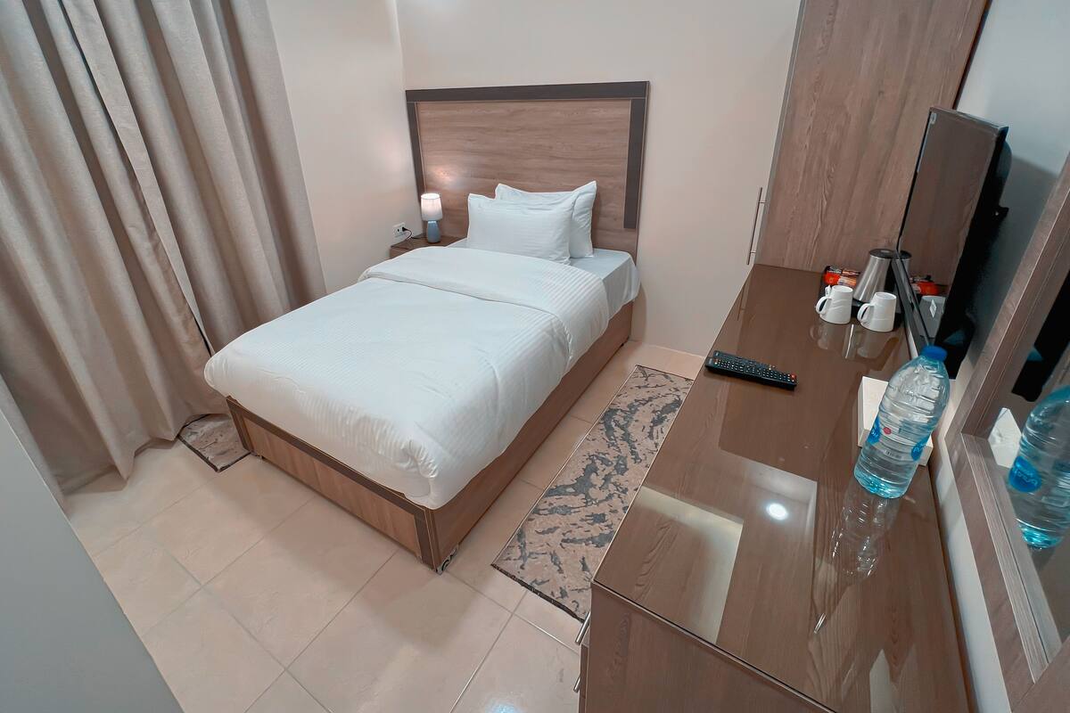 A hotel room with a bed, bedside table, lamp, and a large mirror.