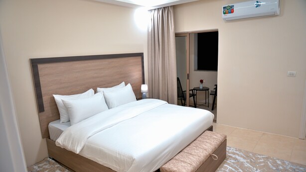 A hotel room with a large bed, a bedside table, a chair, a small table, and an air conditioning unit. - Beit Alshabaan Inn (Wadi Musa)