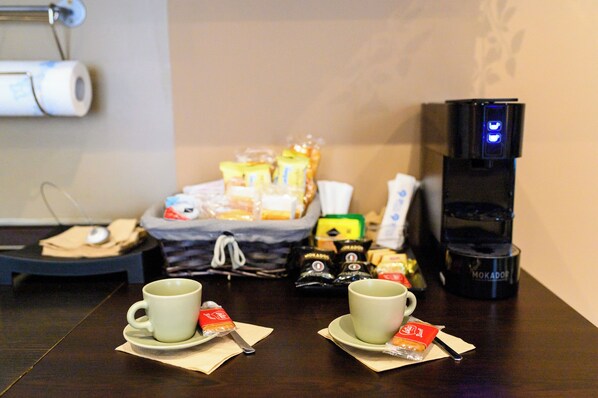 A breakfast setup with two cups of tea, a coffee machine, and various food items on a table.