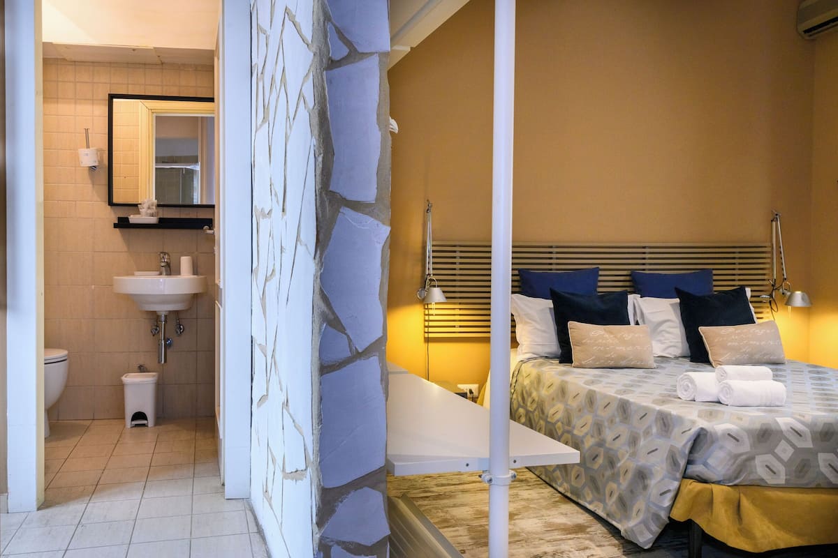 Un bagno con lavandino, wc e specchio. C'è un letto con copriletto e cuscini decorati.