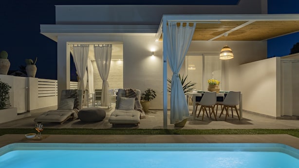A modern outdoor pool area with a seating arrangement, a dining table, and a covered patio.
