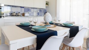 A modern kitchen with white cabinets, a blue tiled backsplash, and a dining area with a white table set for four.