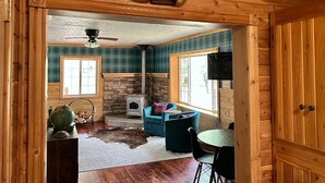 A wooden cabin interior with a stone fireplace, a ceiling fan, a globe, and a deer antler decoration. - Newberry U.P. Cabin (Newberry)