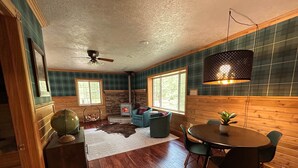 A cozy room with a stone fireplace, wooden walls, a dining table with chairs, and a globe on a dresser. - Newberry U.P. Cabin (Newberry)
