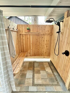 Un espace de douche extérieur en bois, comprenant un banc, un porte-serviettes et un pot de fleurs.