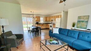 A spacious living area with a blue sofa, a glass coffee table, and a dining table with chairs. - Minutes to Torch Lake | Arcades | AC | Fenced Yard (Rapid City)