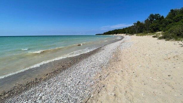 Una playa pedregosa con agua turquesa cristalina y una zona boscosa al fondo.
