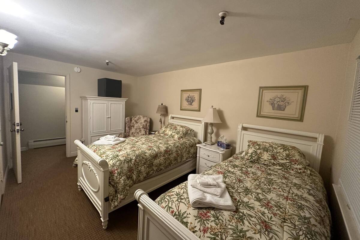 Une chambre avec deux lits, une armoire et une porte donnant sur un couloir.