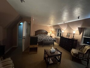 A bedroom with a bed, bedside lamps, a dresser, a chair, and a small table. - The Oaks B&B Hotel and Spiritual Center (Jamestown)