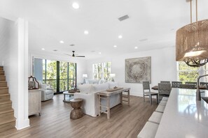 A spacious living room with a wooden floor, a dining area with a long table and chairs, and a staircase with wooden steps.