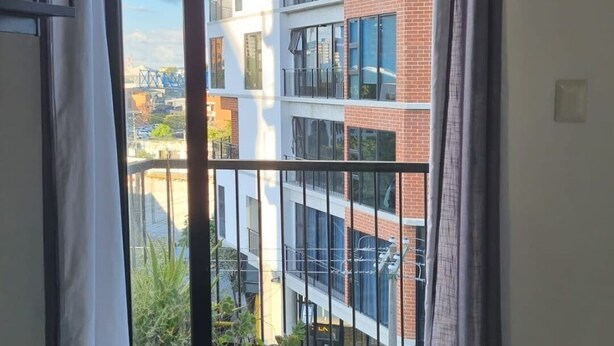 A balcony with a view of a multi-story building, a potted plant, and a hanging towel.