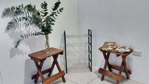 A corner of a room with two wooden tables, one with a vase of green foliage, and a metal drying rack.