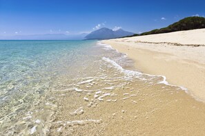 A beach with clear water, a sandy shore, and distant mountains.