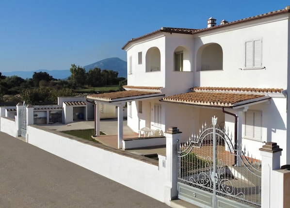 A white villa with multiple balconies, a gated entrance, and a view of a mountain.
