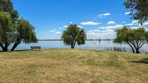 Un espace vert avec de l’herbe, un banc et des arbres, situé près d’un lac paisible.