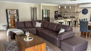 Un salon moderne avec un canapé d’angle, une table basse en bois et un coin cuisine équipé d’un réfrigérateur, d’une cuisinière et de tabourets de bar.