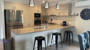 Une cuisine moderne dotée d’appareils électroménagers en acier inoxydable, d’un îlot central avec des tabourets de bar et d’une horloge au mur.