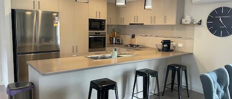 A modern kitchen with stainless steel appliances, a central island with bar stools, and a clock on the wall.