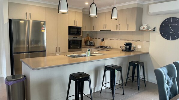 A modern kitchen with stainless steel appliances, a central island with bar stools, and a clock on the wall.