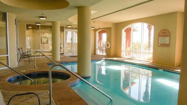 An indoor swimming pool with clear pool rules posted, a sunlit room with large windows, and a view of the outdoors. - Gorgeous Beachfront Condo with 
ocean views (Gulfport)