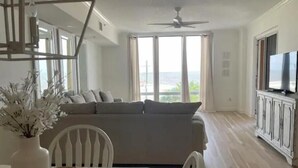 A modern living room with a sofa, a dining table with chairs, a TV, and a view of the outdoors. - Gorgeous Beachfront Condo with 
ocean views (Gulfport)