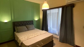 A bedroom with a bed, a hanging light fixture, a window with curtains, and an air conditioning unit. - Oasis by Franklin #9 (La Fortuna)