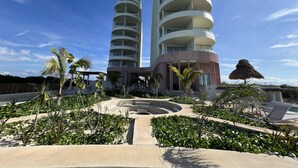 A modern hotel with a circular design, featuring a pool area with lounge chairs and tropical plants.