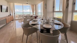 A dining area with a view of the ocean, a ceiling fan, and a television on the wall.