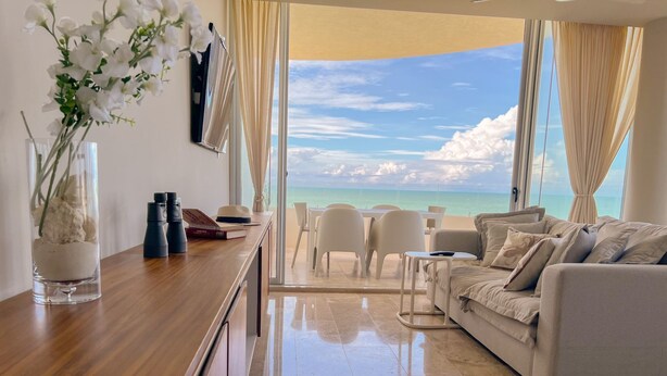 A modern living room with a view of the ocean, a dining area, and a large window with curtains.