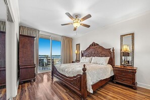 Ein geräumiges Schlafzimmer mit einem großen Bett, einem Deckenventilator, einem Nachttisch, einer Kommode und einem Balkon mit Blick.