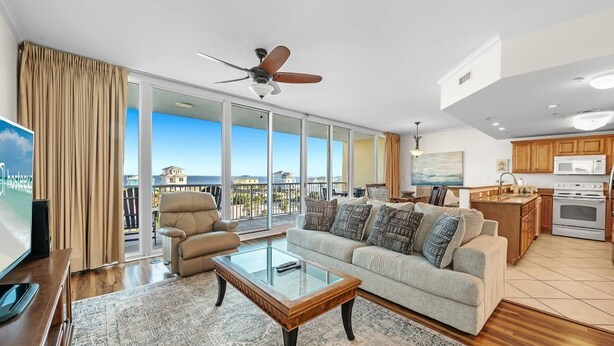 Un salon spacieux comprenant un canapé, une table basse et un téléviseur. Un balcon avec vue sur la mer est visible à travers de grandes fenêtres.