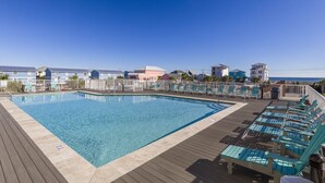 Une piscine dotée de chaises longues et d’une terrasse en bois, entourée de bâtiments offrant une vue dégagée sur l’océan.