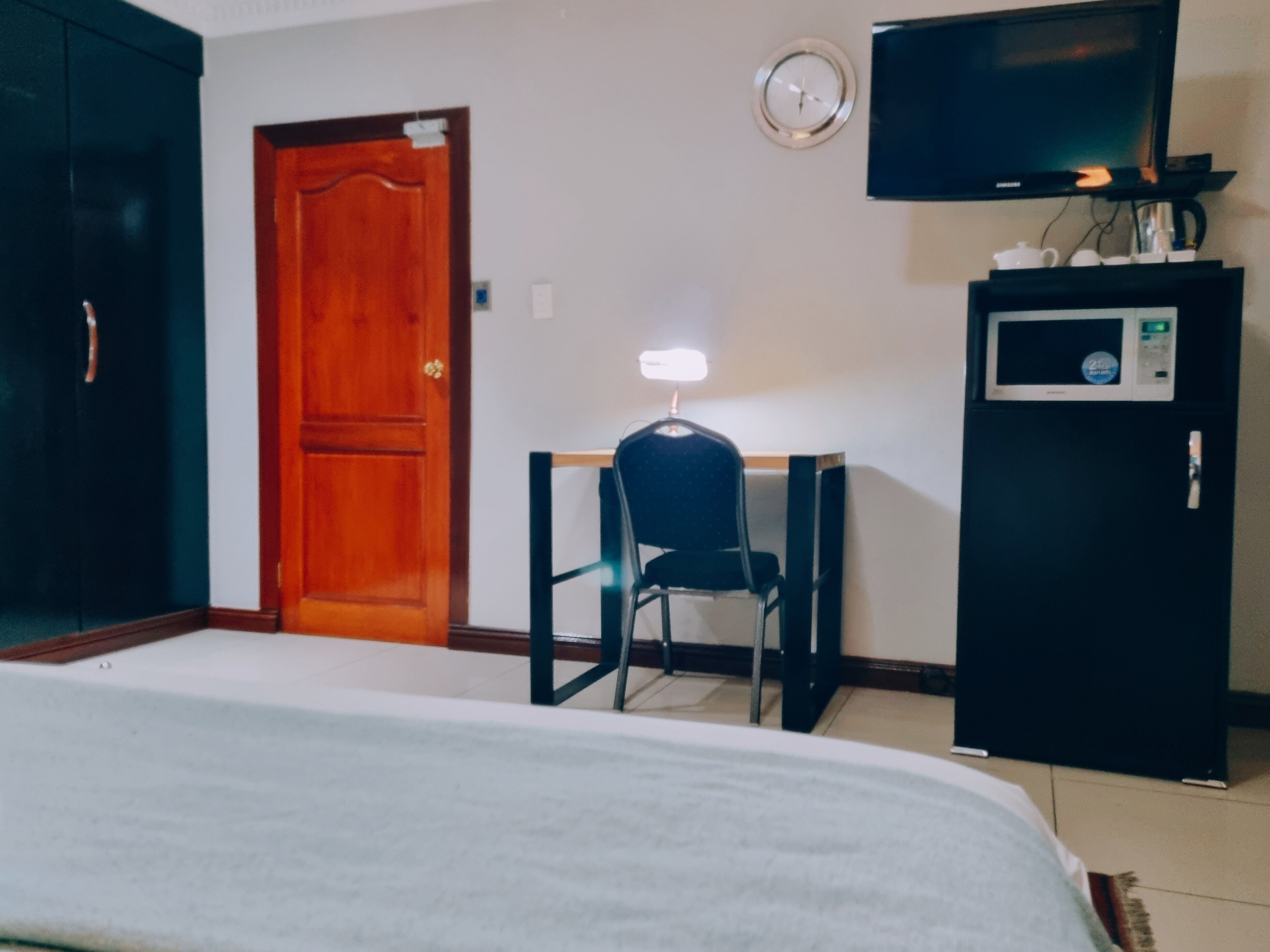 A room with a bed, a desk with a chair, a television, and a refrigerator.