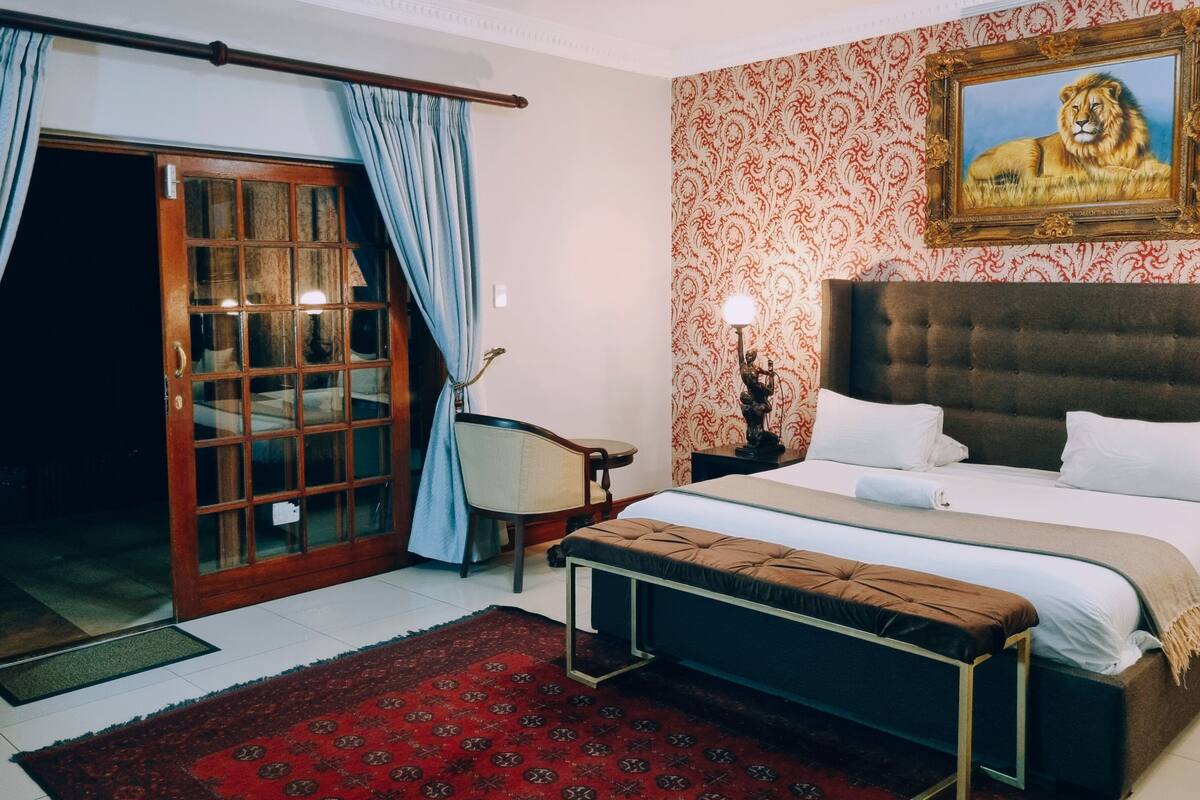 Un dormitorio con una cama grande, un banco, una silla, una puerta con paneles de vidrio y una pared con diseño.