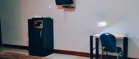 A hotel room with a bed, a desk with a chair, a television mounted on the wall, and a clock.